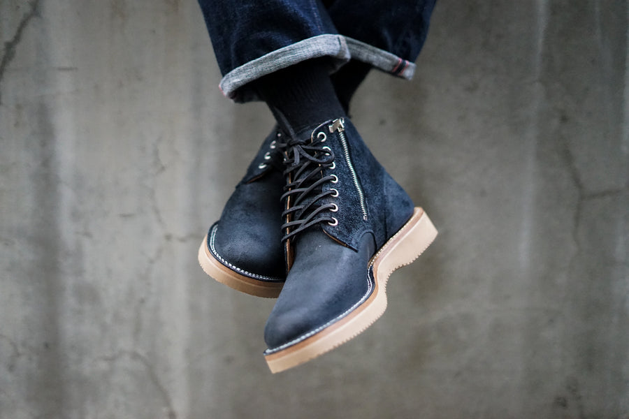Two feet wearing the boots over a ledge are crossed, showing off the nickel side zipper on the inside of the boot.