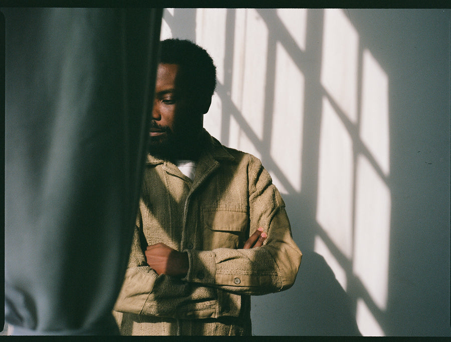 A man in a tan shirt stands behind a curtain