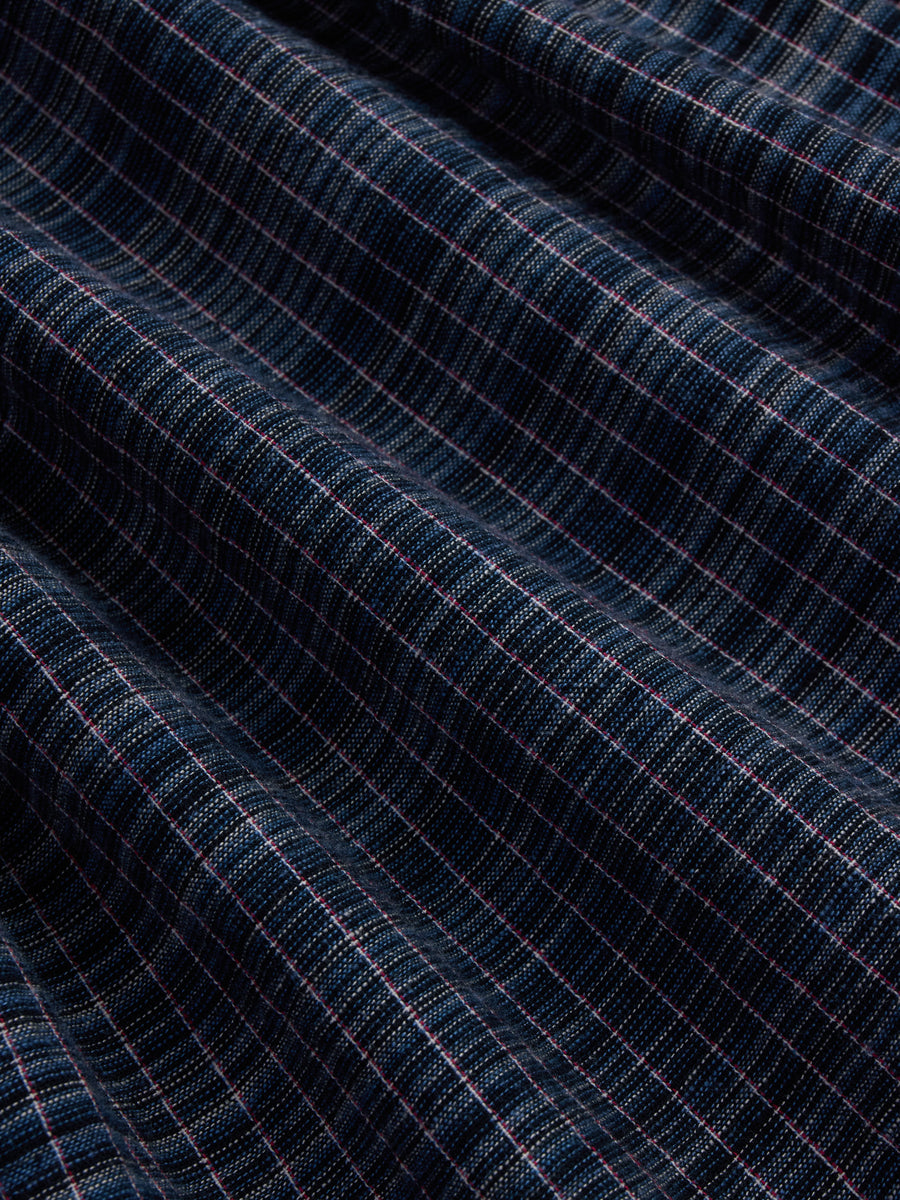 A close-up of dark navy blue fabric with a fine pink and white windowpane plaid pattern, showing soft folds and texture.