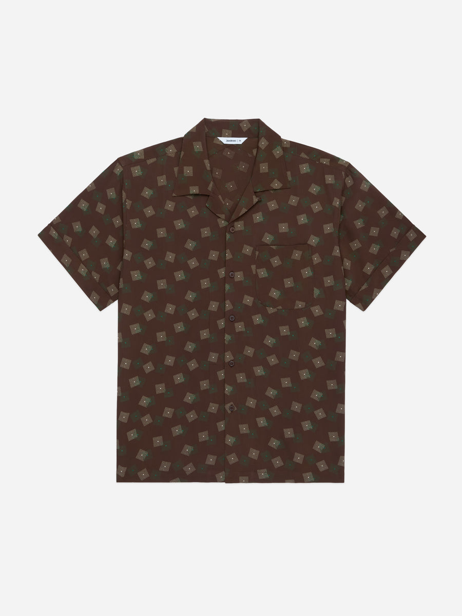 A short-sleeve button-up camp shirt in dark brown with an all-over beige geometric pattern, displayed flat against a light gray background.