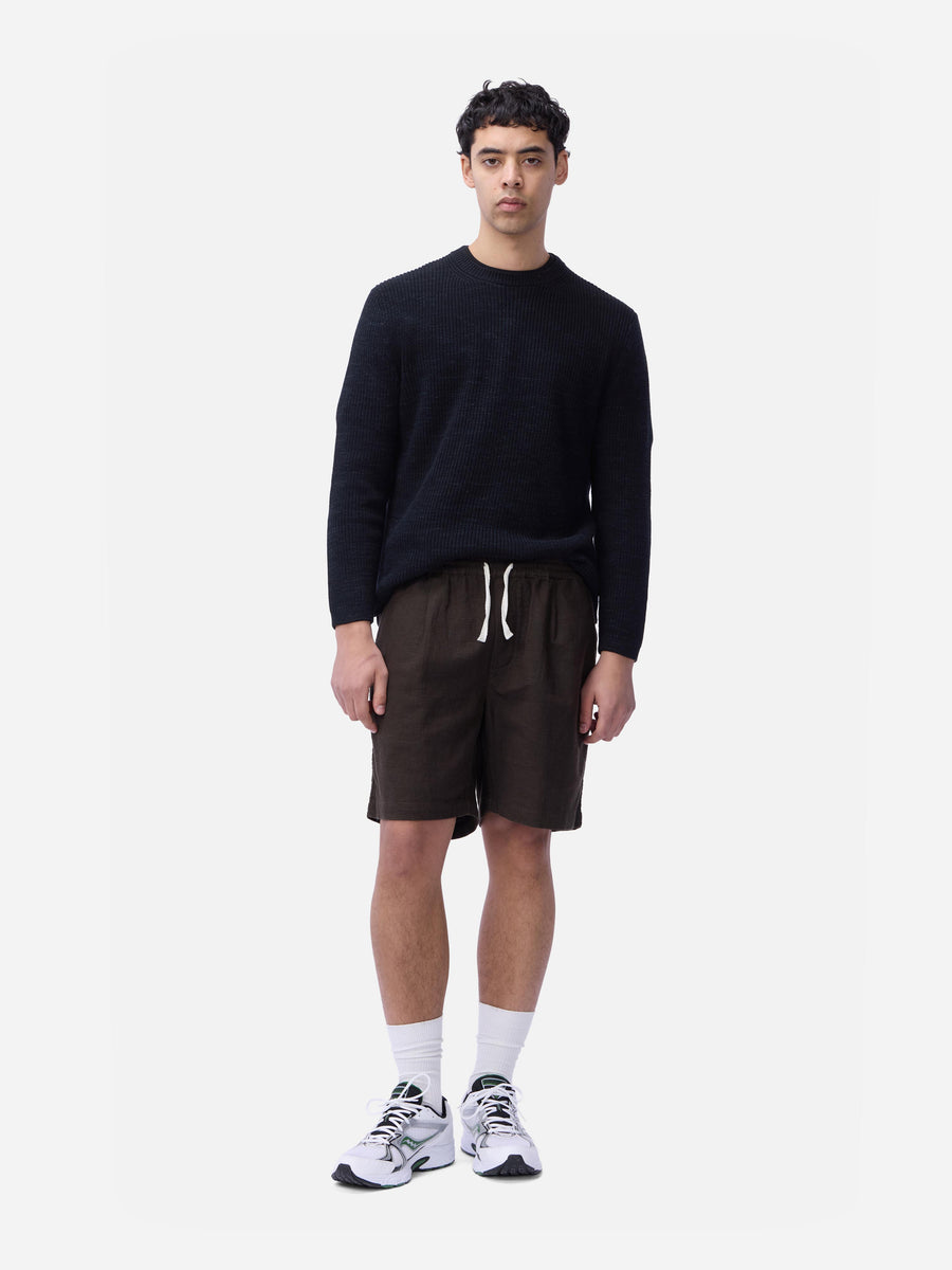 Man wearing a black sweater, brown shorts, and white sneakers on a white background