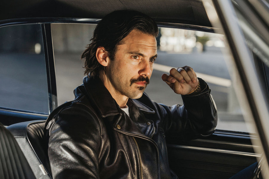 Model wearing a leather jacket while posing inside of a car.