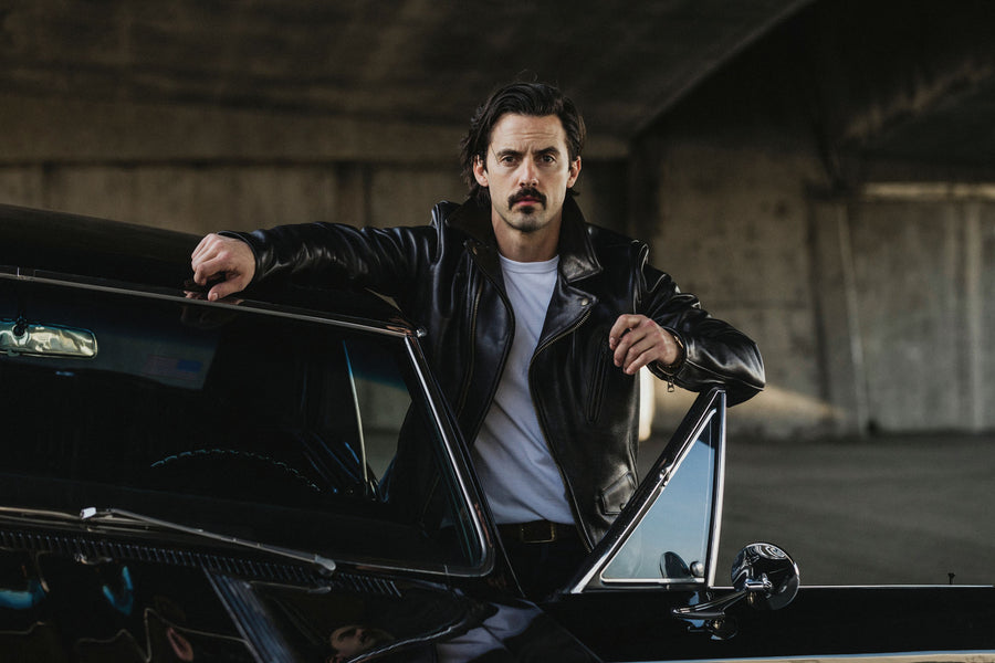 Model standing behind an open car door while wearing a leather jacket.