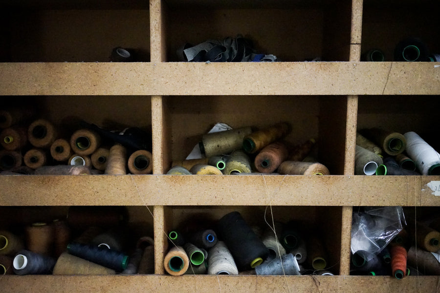 Various spools of thread used to sew denim sit in different bins, sorted by colors.