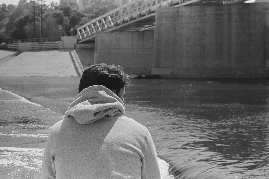 A man in a grey hoody looks at a river.