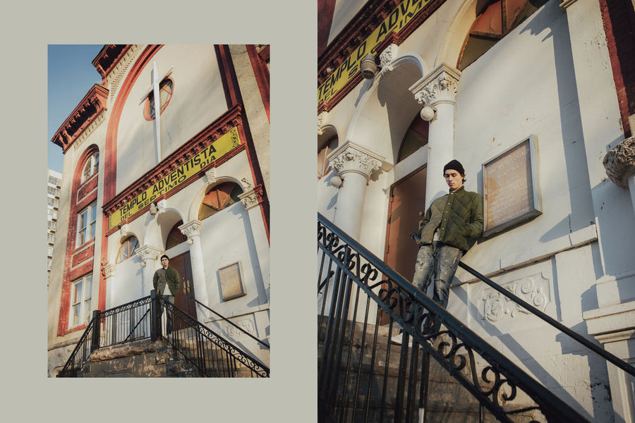 A model poses with an olive patchwork down jacket on while standing on the steps of a church.