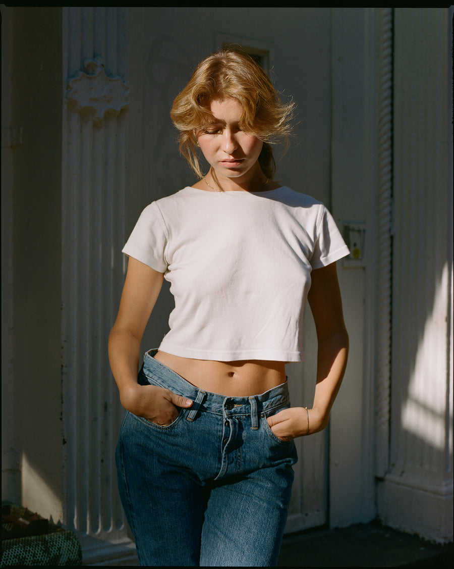 A lady in a white tee and light blue jeans in the sunset.