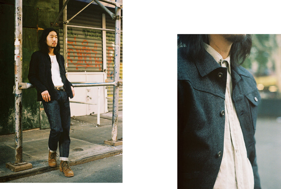 The model leans against some scaffolding wearing a black 3sixteen shirt and indigo jeans.